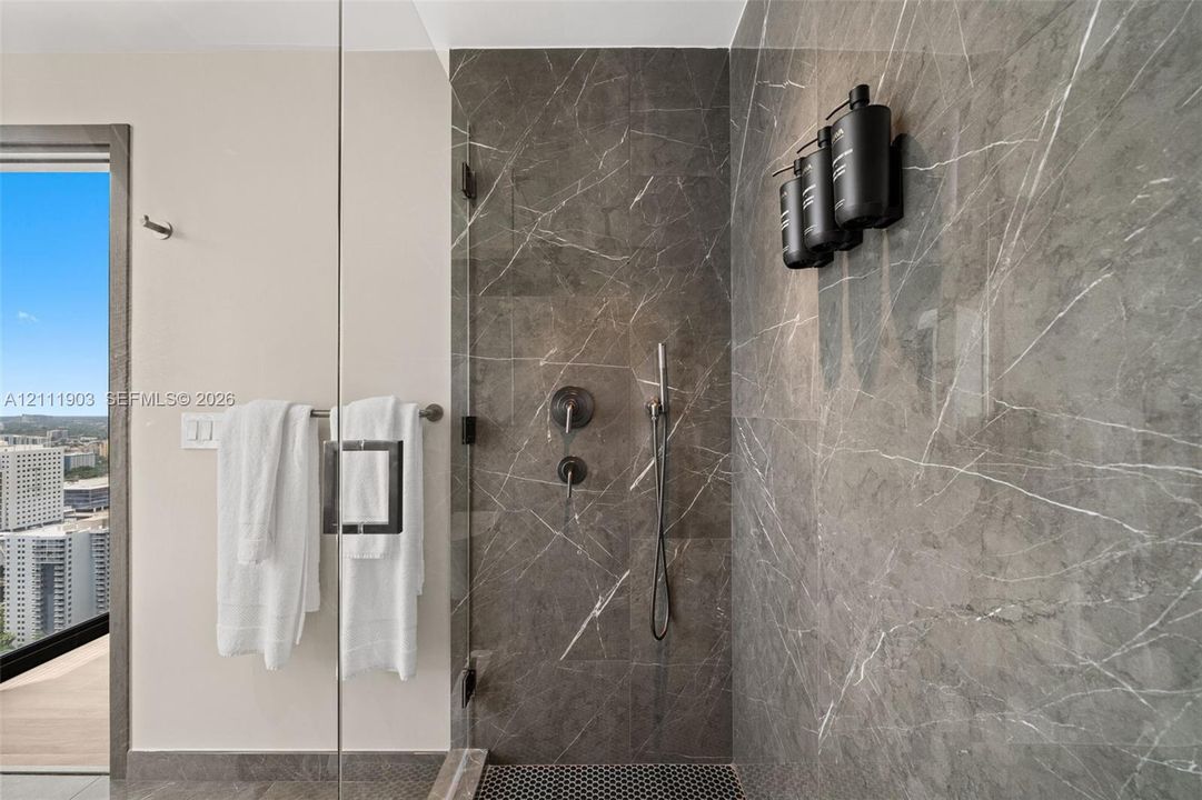 Walk-in shower featuring floor-to-ceiling stone-finish tile, frameless glass enclosure, dark-finish wall-mounted shower hardware, and mosaic tile flooring