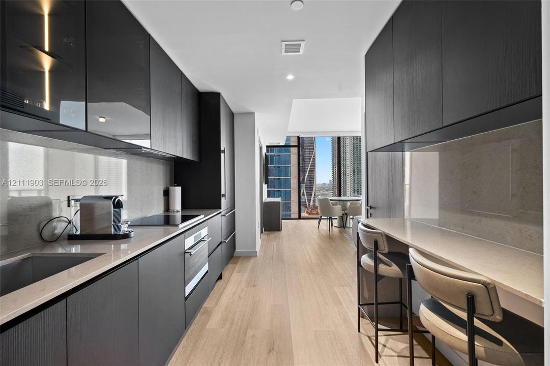 Kitchen featuring matte dark cabinetry, light-toned stone countertops, integrated appliances, wood-finish flooring, and a built-in breakfast bar