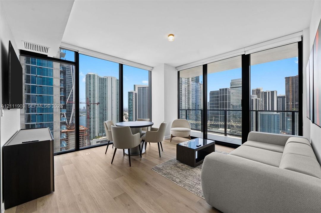 Floor-to-ceiling windows with panoramic urban skyscraper scenery, wood-finish flooring, and recessed ceiling lighting