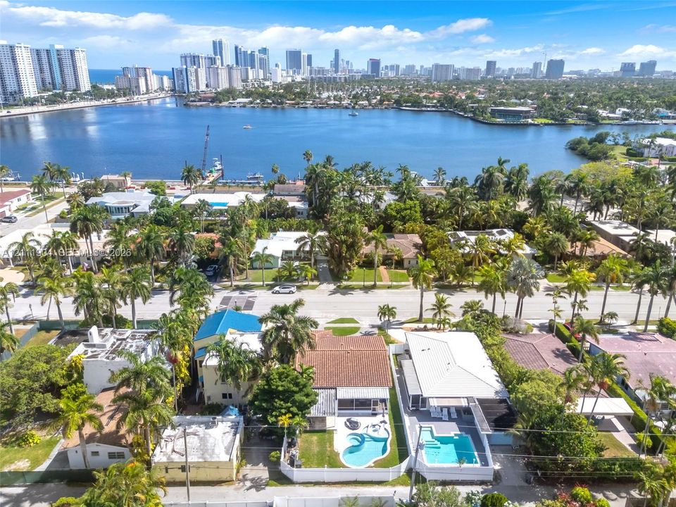 Aerial perspective of a coastal residential neighborhood featuring mature palm trees and direct proximity to the intracoastal waterway and city skyline