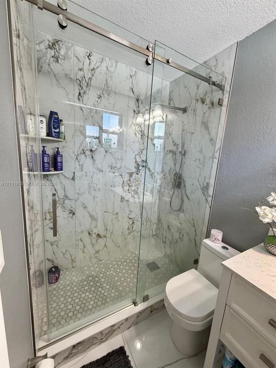 Walk-in shower featuring large-format patterned tile walls, a sliding glass door with brushed metal hardware, a handheld shower fixture, and a mosaic hexagonal tile floor