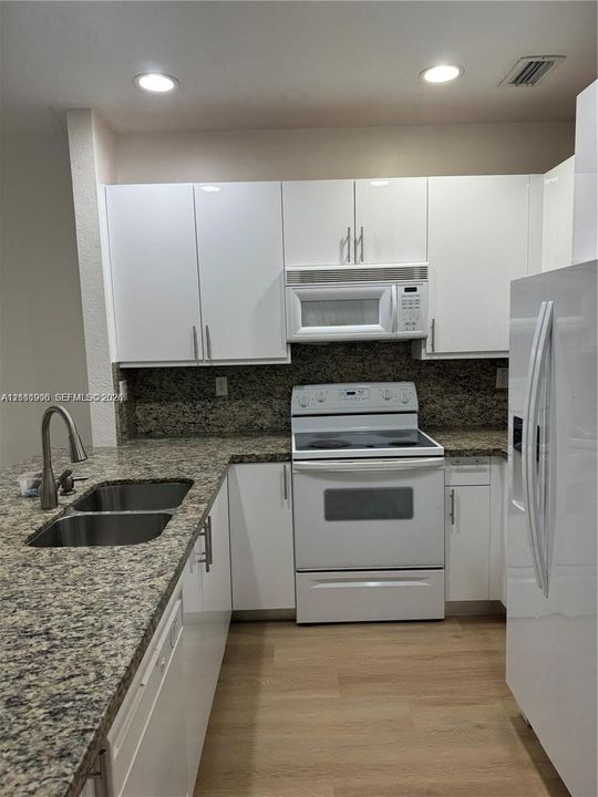 Kitchen featuring white cabinetry, stone-surface countertops, dual-basin stainless steel sink with high-arc faucet, integrated appliances, and wood-finish flooring