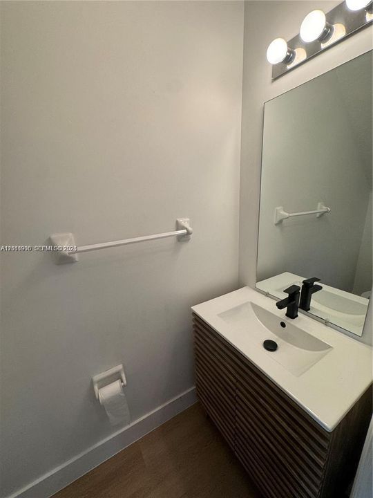 Slatted wood-finish vanity with a rectangular sink, integrated white countertop, matte black faucet, and frameless wall mirror