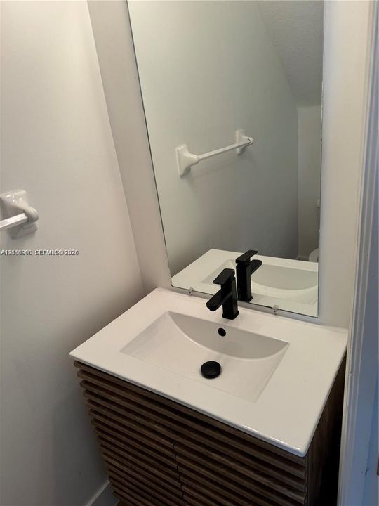 Slatted wood-finish vanity with a rectangular integrated sink, white composite countertop, and matte black faucet, featuring a large frameless wall mirror