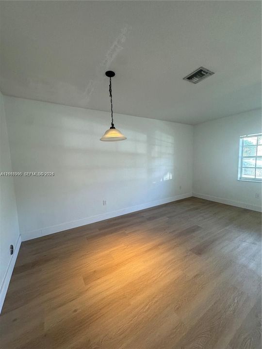 Interior space featuring wood-finish flooring, a neutral color palette, a single-pane window, and a suspended pendant light fixture