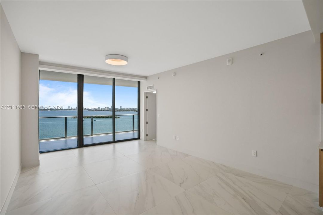 Floor-to-ceiling glass sliding doors, large-format tiled flooring, neutral wall finishes, flush-mount circular lighting, and metal-railing balcony