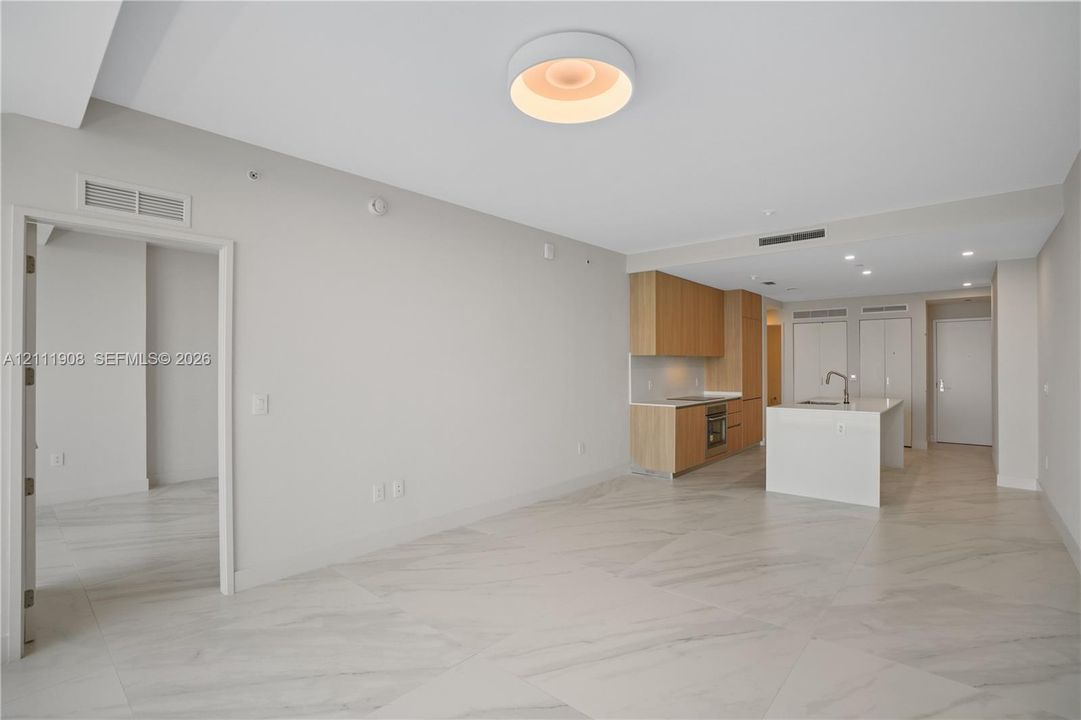 Open-concept living space featuring large-format tile flooring, a kitchen island with a built-in sink, flat-panel cabinetry, and modern circular ceiling lighting