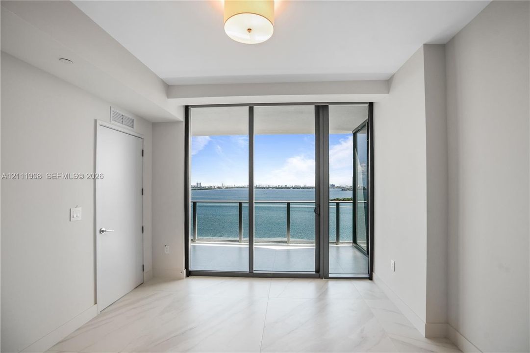 Floor-to-ceiling sliding glass doors, private balcony with metal railing, neutral tile flooring, and flush-mount drum ceiling light