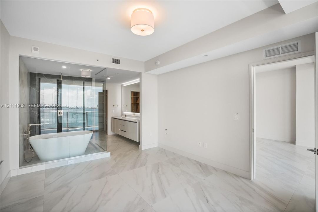 Glass-enclosed wet room featuring a freestanding soaking tub, large-format tile flooring, double-sink vanity with under-cabinet lighting, and flush-mount drum lighting
