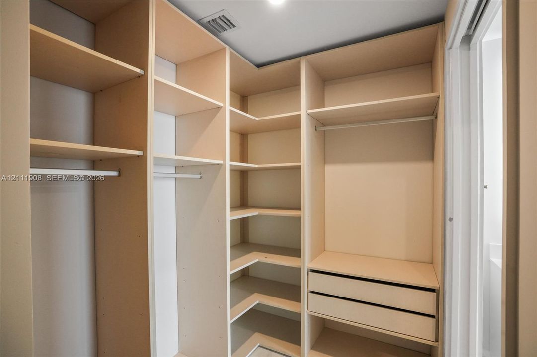 Custom storage system featuring floor-to-ceiling wooden shelving, integrated hanging rods, and two soft-close drawers