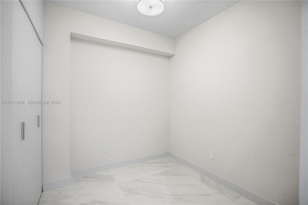Interior space featuring large-format stone-finish floor tiling, crisp neutral wall paint, ceiling-mounted flush lighting, and floor-to-ceiling sliding closet doors with metallic hardware