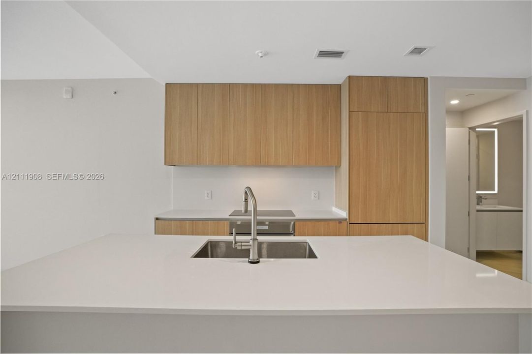 Kitchen featuring light wood-finish cabinetry, a white stone countertop island, an undermount stainless steel sink with a gooseneck faucet, and integrated appliances