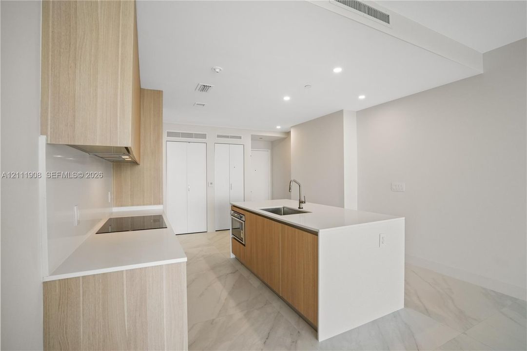 Kitchen featuring wood-finish cabinetry, an island with a stone-surface countertop, an integrated electric cooktop, and large-format tile flooring