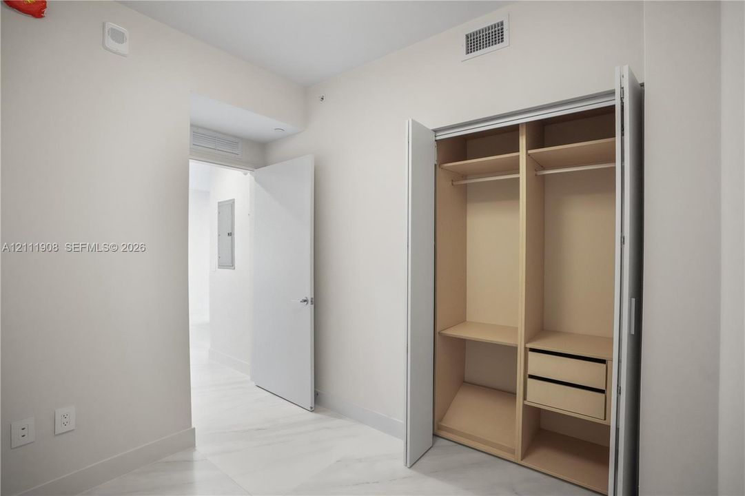 Built-in closet featuring dual hanging rods, fixed shelving, and integrated drawer storage, complemented by stone-finish flooring and solid core swing doors