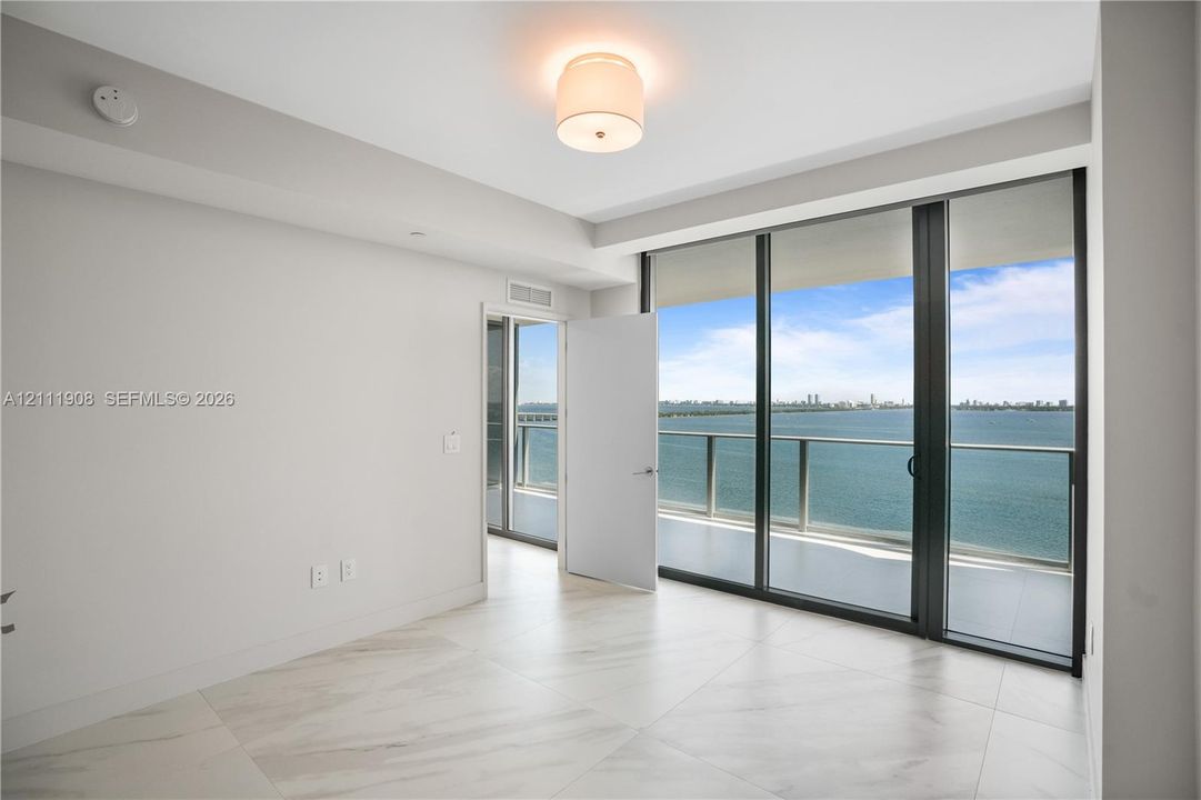 Floor-to-ceiling glass sliding doors, large-format tile flooring, metal-frame balcony railing, and recessed ceiling lighting