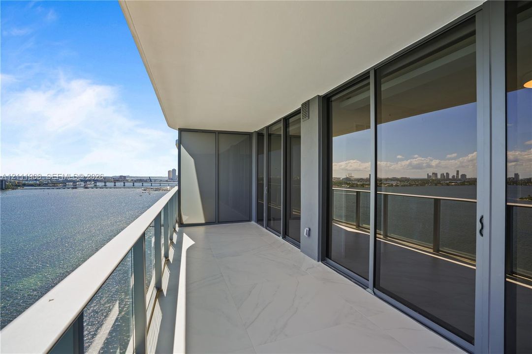 Covered balcony with large-format tile flooring, tempered glass railings, and floor-to-ceiling sliding glass doors