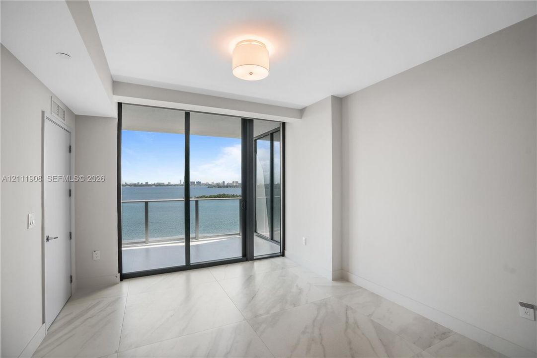 Floor-to-ceiling sliding glass doors, private balcony, large-format tile flooring, and overhead flush-mount lighting