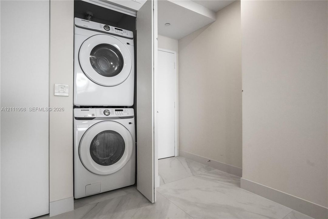 Stacked laundry center with high-capacity washer and dryer, finished with large-format tile flooring and neutral wall paint