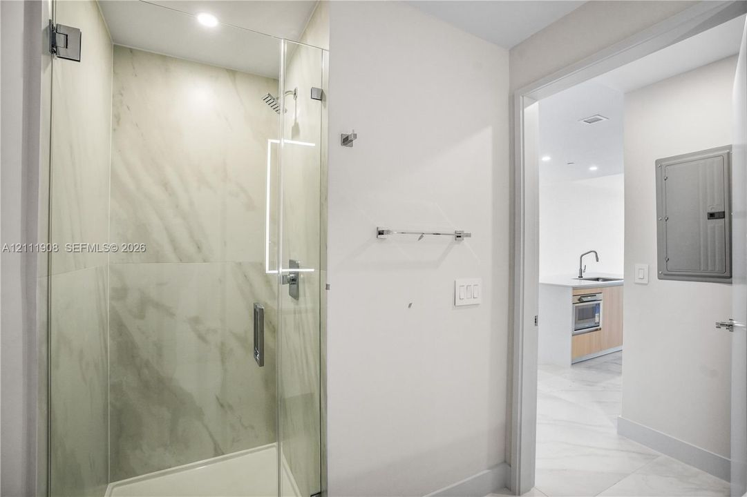 Walk-in shower featuring large-format stone-patterned tile, frameless glass enclosure, and recessed lighting