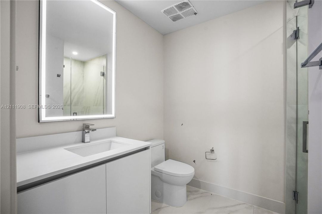 Modern vanity featuring a stone countertop, integrated sink, and wall-mounted, back-lit mirror
