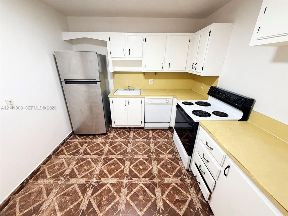 Kitchen featuring white cabinetry, solid-surface countertops, tile flooring, and integrated appliances