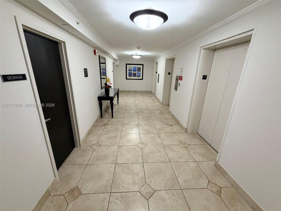 Hallway featuring neutral tile flooring with diamond-patterned inlay, ceiling-mounted dome lighting, and multiple elevator access points