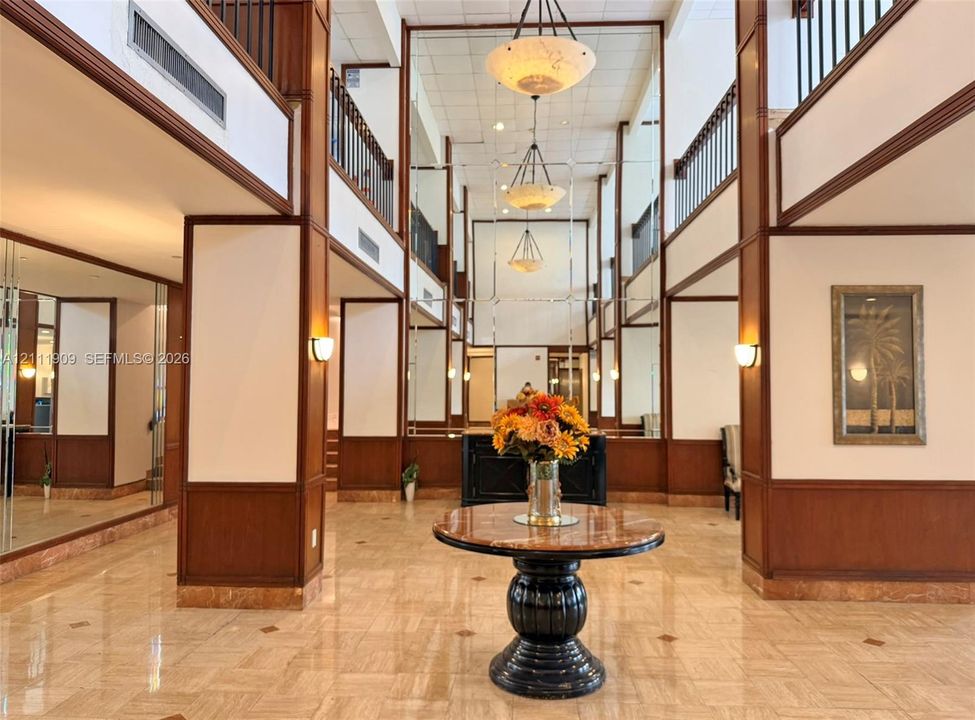 Multi-story lobby featuring stone flooring, full-height mirrored wall panels, wood-trimmed architectural columns, tiered pendant lighting, and metal balcony railings