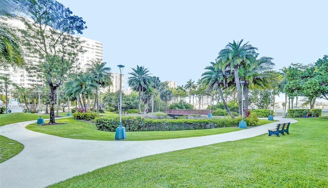 Landscaped grounds featuring winding concrete pathways, mature palm trees, decorative shrubbery, and a wooden pedestrian bridge