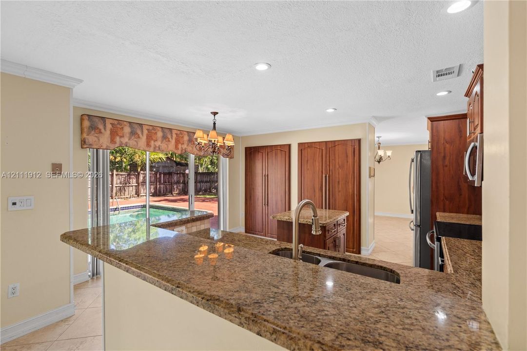 Kitchen featuring a wrap-around stone countertop, recessed lighting, built-in wooden cabinetry, stainless steel sink with gooseneck faucet, and sliding glass doors