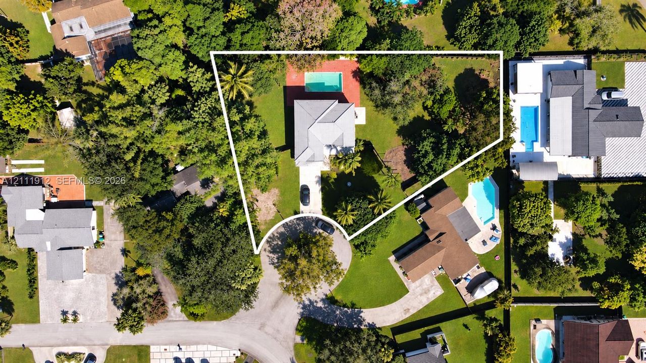 Aerial perspective of a property featuring an in-ground swimming pool, expansive grounds, mature trees, and a paved driveway