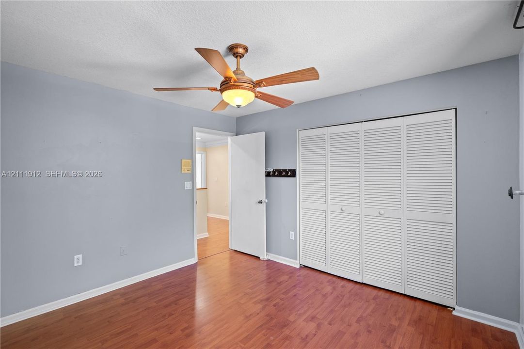 Room featuring wood-finish flooring, a ceiling fan with integrated lighting, and a four-panel louvered closet door