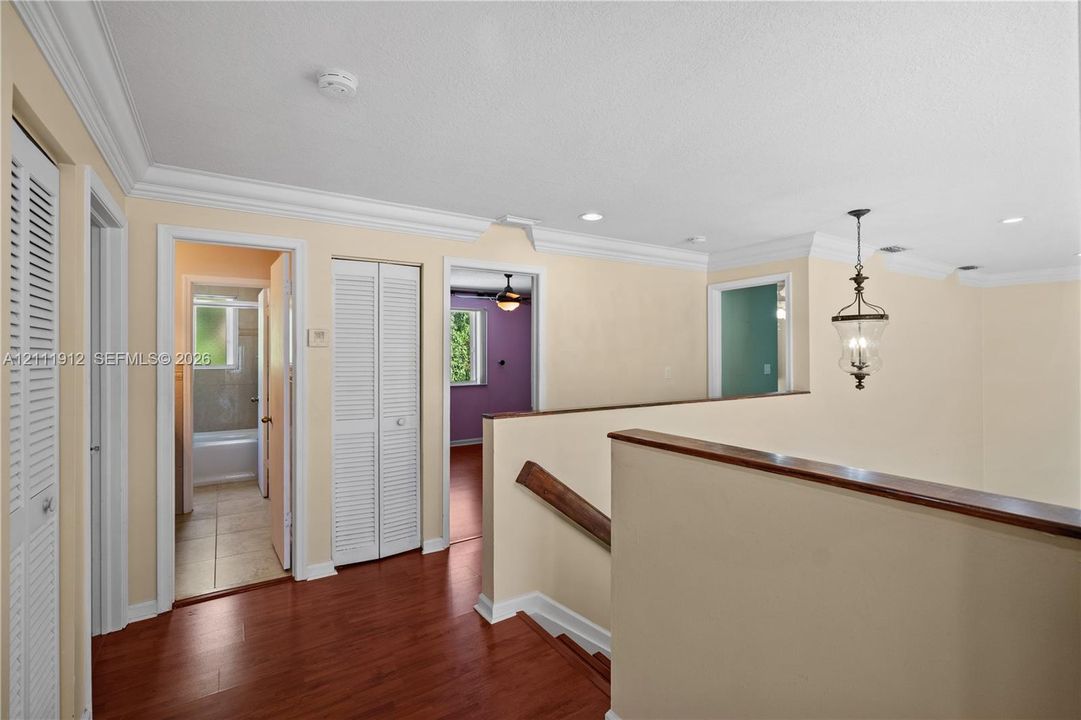 Hallway featuring wood-finish flooring, crown molding, louvered closet doors, and a hanging lantern-style light fixture
