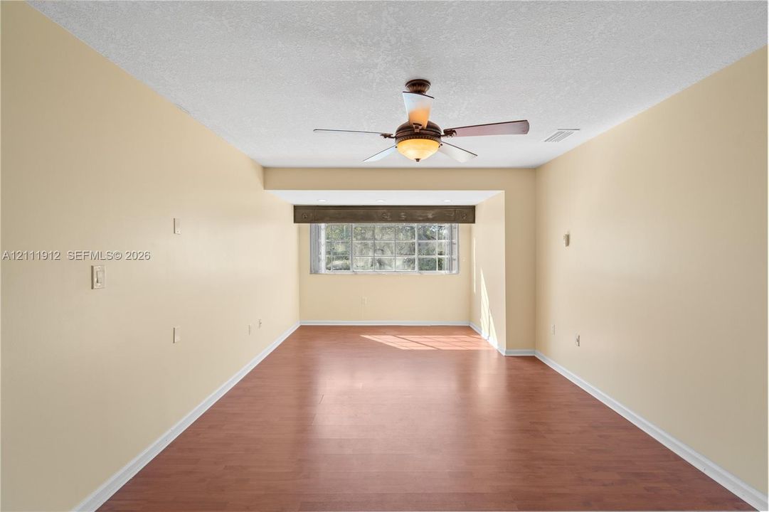 Interior room featuring wood-finish flooring, a multi-pane window with a decorative valance, and a ceiling-mounted light fixture with integrated fan blades
