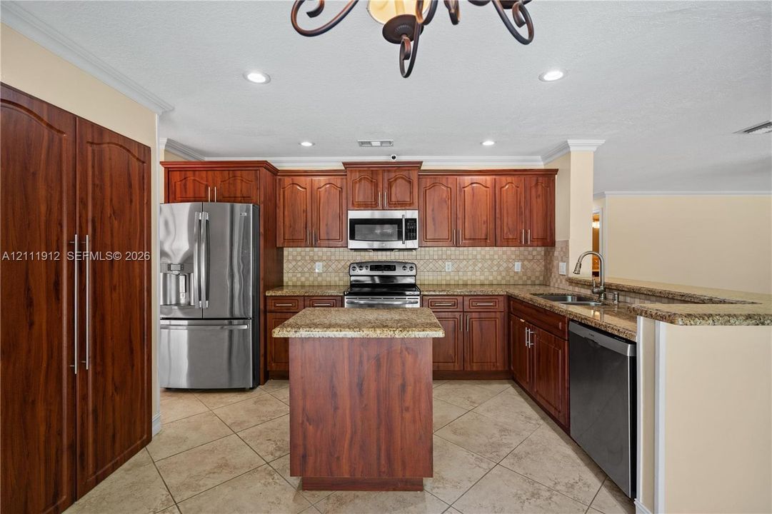 Kitchen featuring cherry-finish cabinetry, stainless steel appliances, stone-surface countertops, a center island, and tile flooring