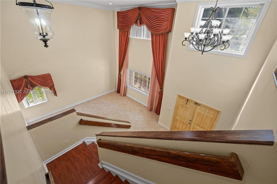 Double-height foyer featuring a staircase with wood-finish handrails, tile flooring, and multi-tiered decorative chandeliers