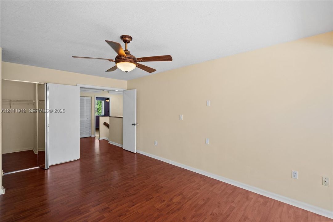 Room featuring wood-finish flooring, a ceiling fan with integrated lighting, and a closet with mirrored doors
