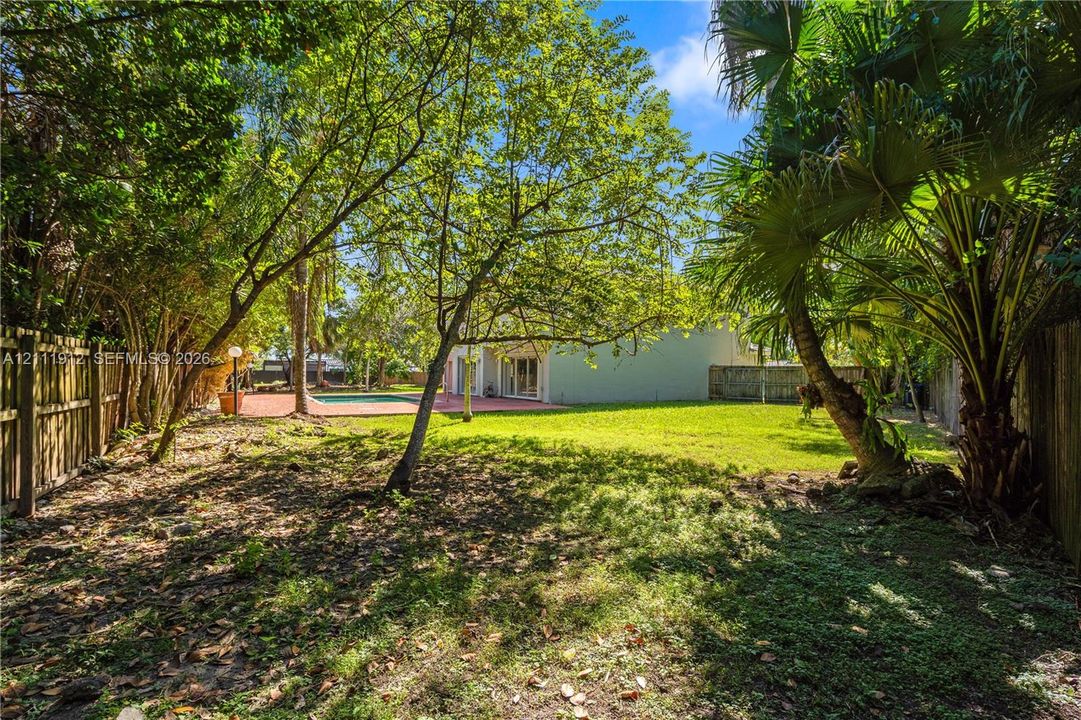 Expansive backyard featuring mature trees, a manicured lawn, a swimming pool, a paved patio area, and wood fencing