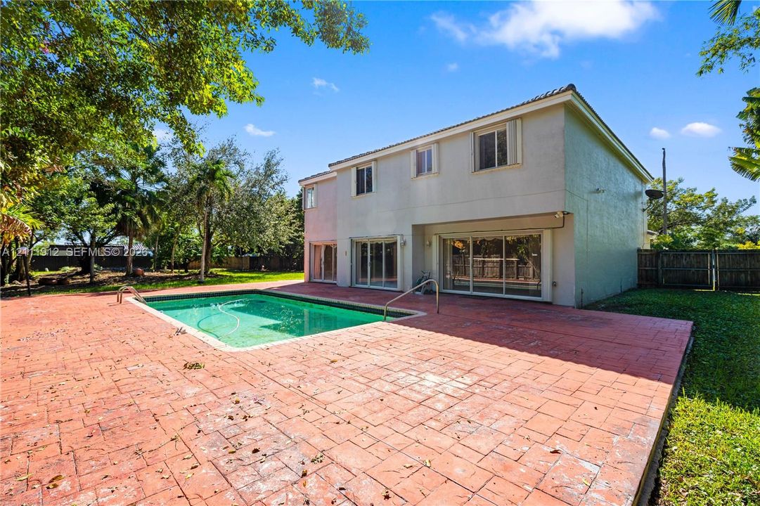 Two-story residence featuring an in-ground swimming pool, expansive stamped concrete patio, sliding glass doors, and mature landscaping