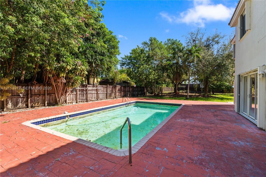 In-ground swimming pool featuring a tiled waterline, surrounded by an expansive paved patio and a wood-slat privacy fence