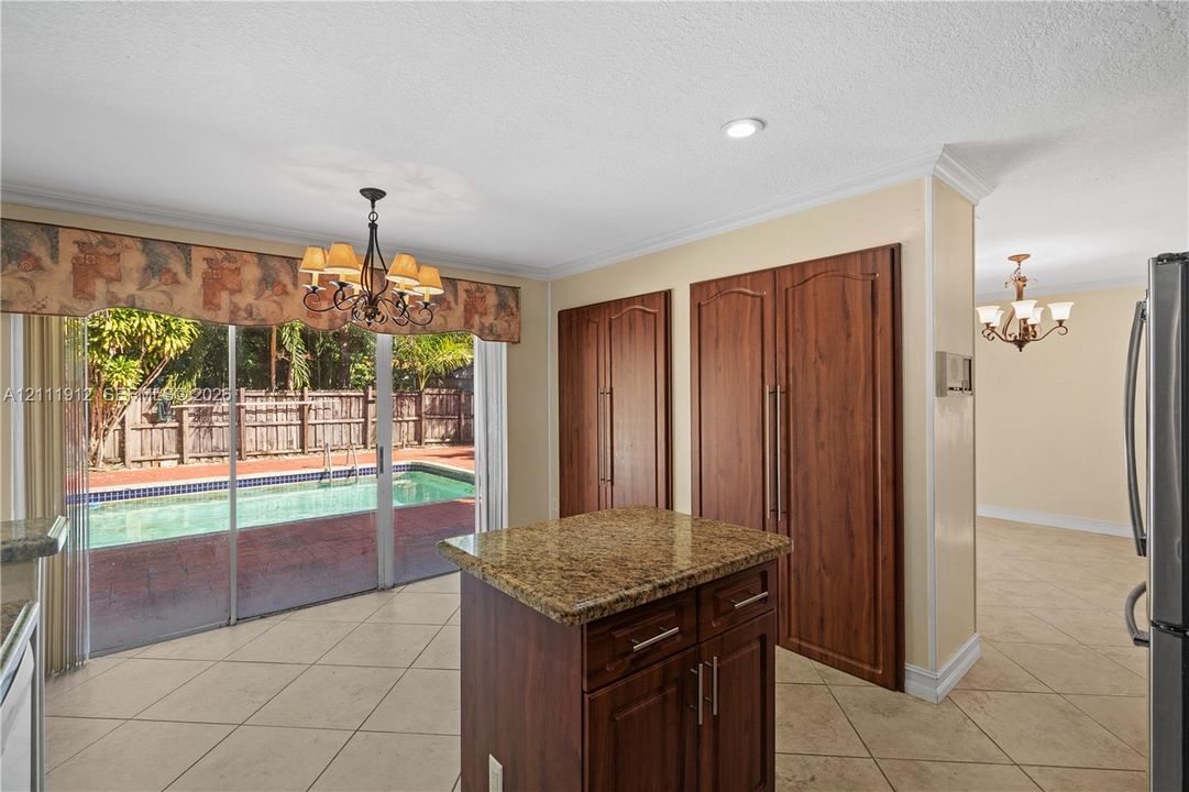 Kitchen featuring a center island with a natural stone countertop, full-height wood cabinetry, neutral tile flooring, and sliding glass doors opening to an exterior swimming pool
