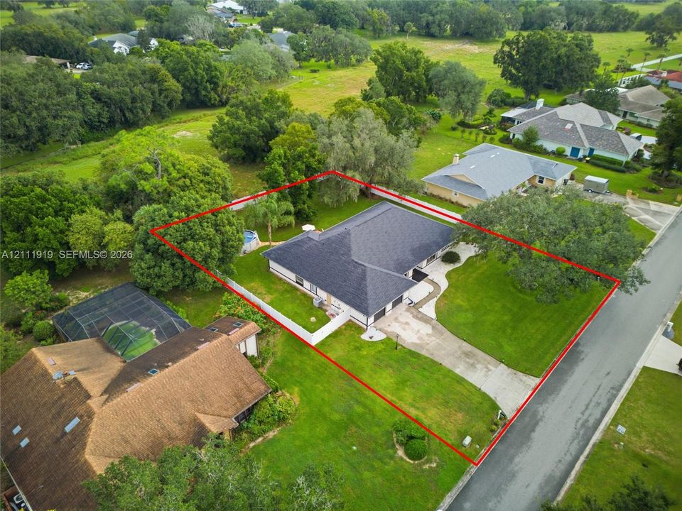 Single-story residence featuring a hipped roof, attached multi-car garage, concrete driveway, and expansive lawn with mature trees