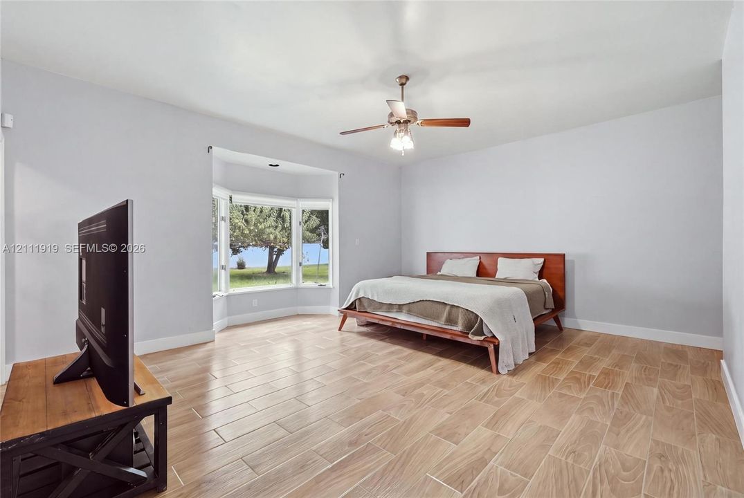 Spacious room featuring wood-finish flooring, a prominent bay window, and a ceiling-mounted light fixture with a central fan
