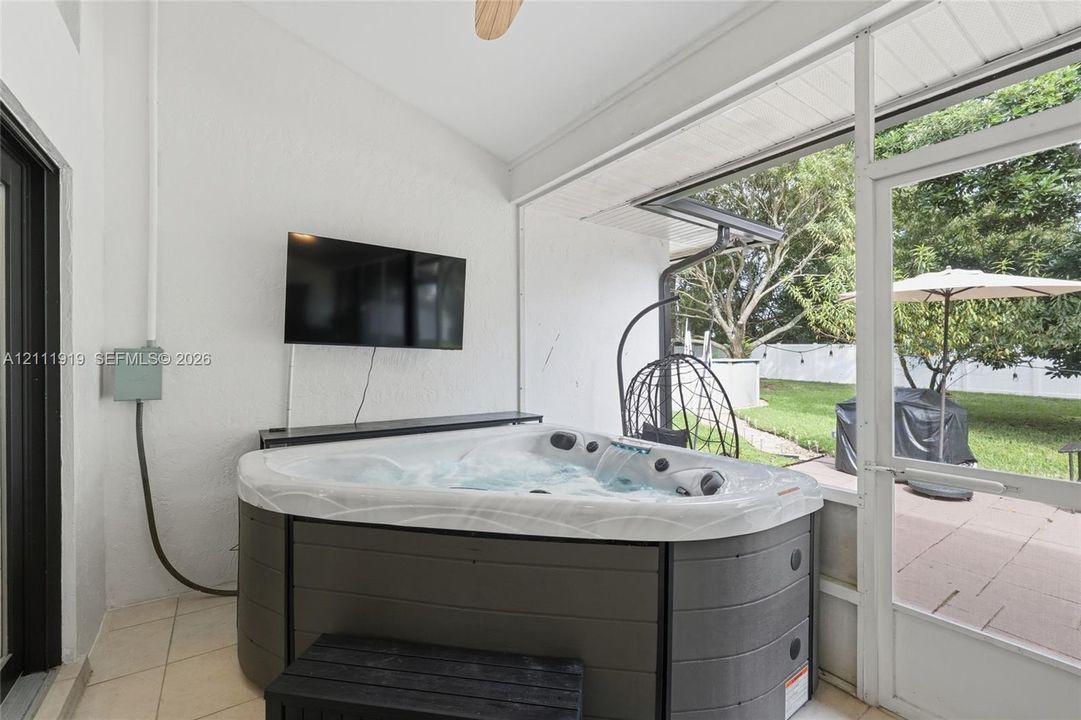 Screened-in patio featuring tile flooring, ceiling fan, and built-in hot tub