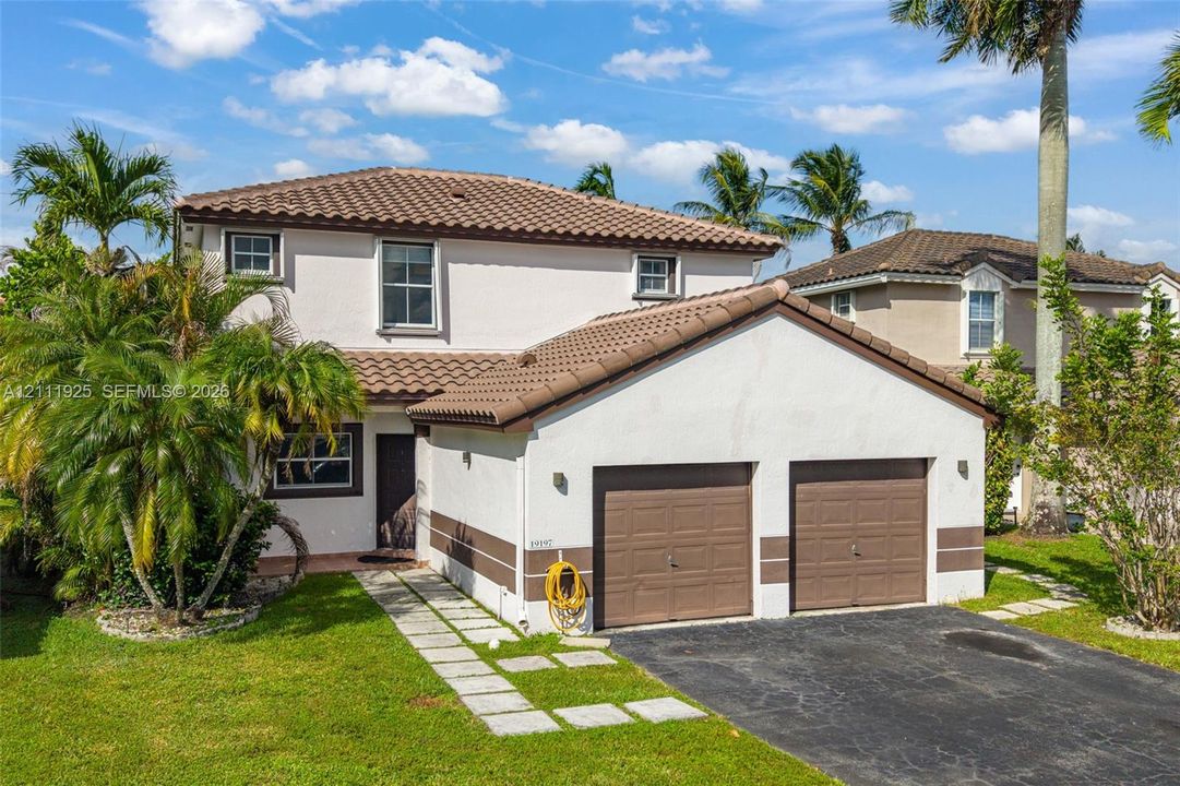 Two-story residence with a stucco exterior, tiled roof, two-car garage, and stone-paver walkway