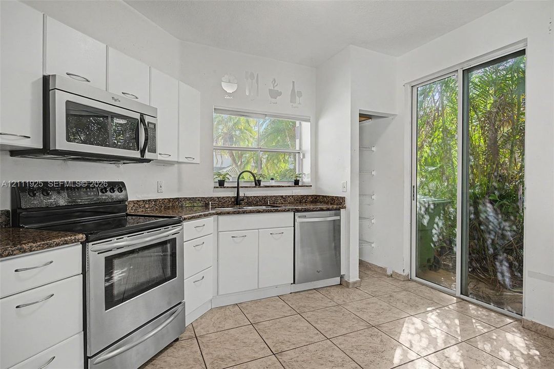 Kitchen featuring white cabinetry, stone-finish countertops, stainless steel appliances, ceramic tile flooring, and sliding glass doors