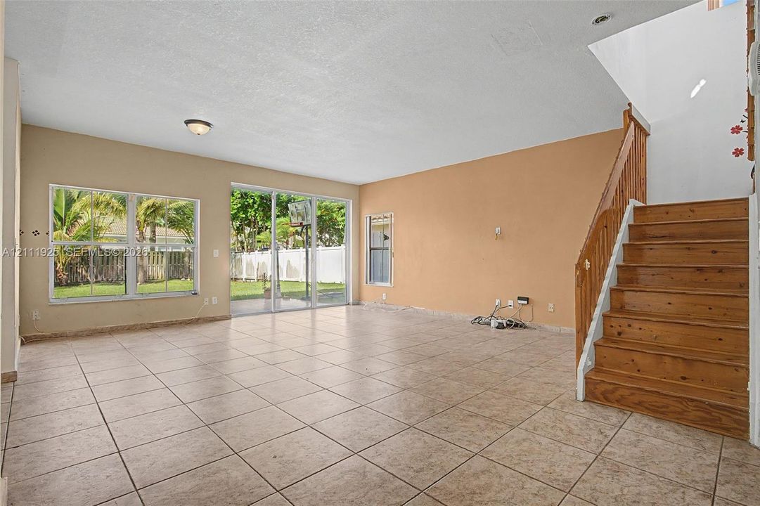 Open interior featuring ceramic tile flooring, sliding glass patio doors, natural light, and a wooden staircase with a matching handrail