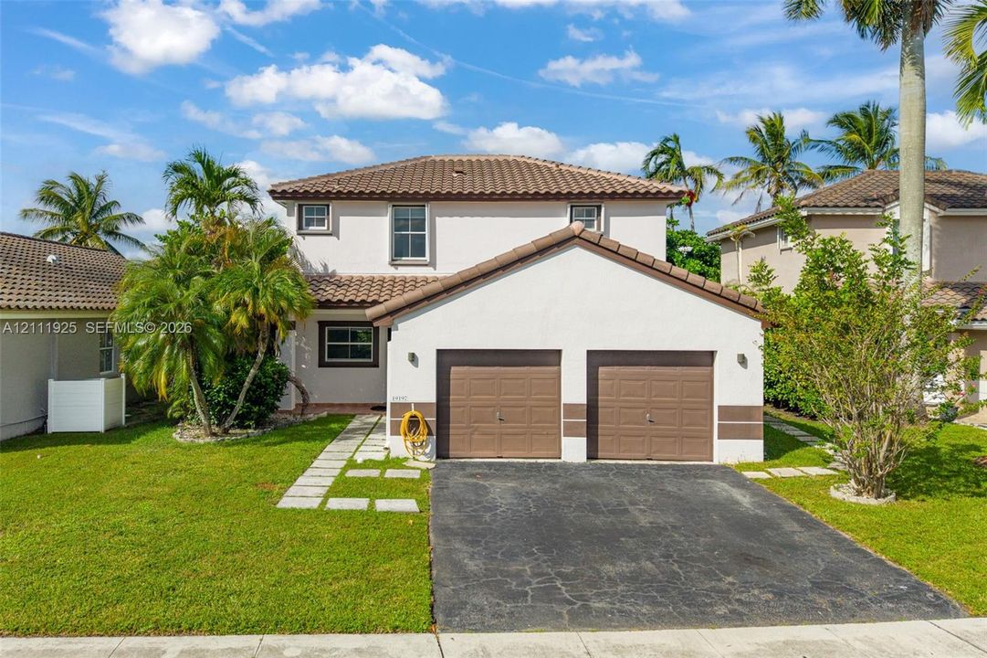 Two-story stucco exterior featuring a tiled hip roof, two-car garage with sectional doors, and decorative masonry accents
