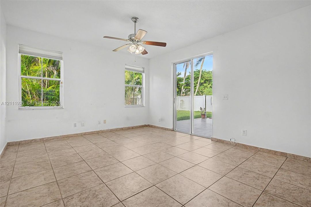 Interior space featuring neutral tile flooring, two multi-pane windows, ceiling fan with integrated lighting, and a sliding glass door