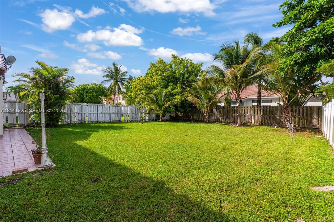 Expansive backyard featuring a large grass lawn, perimeter wood fencing, mature palm trees, and a paved patio area