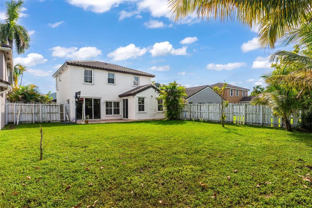 Expansive backyard featuring a manicured lawn, perimeter wood fencing, and mature palm trees